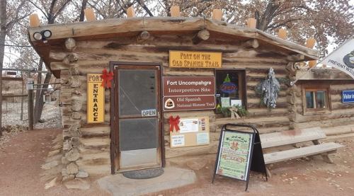 Log cabin entrance of Fort Uncompahgre, decorated for the holidays, with signs for the interpretive site and trails.