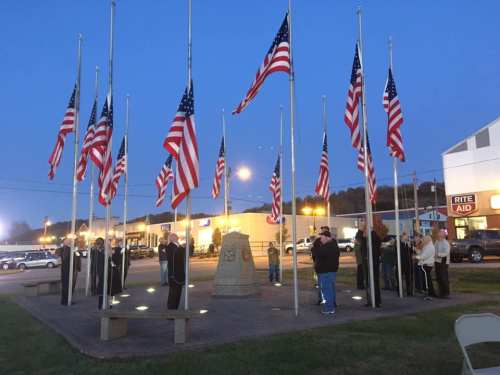 A group of people gathered around a monument surrounded by American flags at dusk.