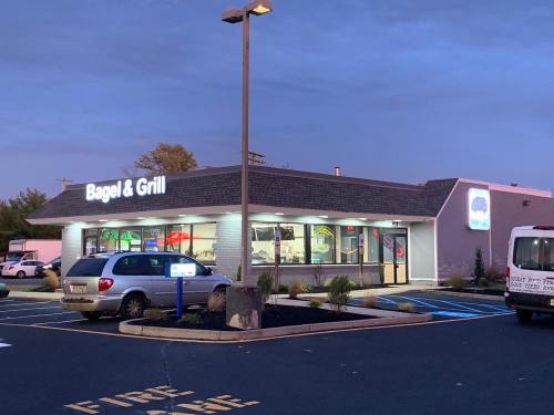 Exterior of Bagel & Grill restaurant at dusk, featuring a parking lot and illuminated signage.