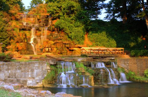 A serene waterfall cascading over rocks, surrounded by lush greenery and a wooden viewing platform.