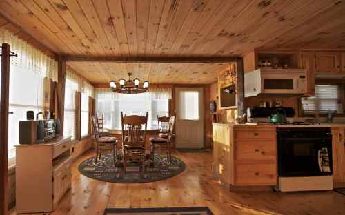 Cozy wooden kitchen and dining area with a round table, chairs, and large windows letting in natural light.