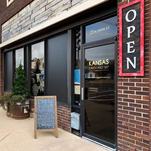 Exterior of a shop named "Kansas Earth and Sky," featuring a sign that says "Open" and a chalkboard with a message.