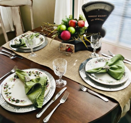 A beautifully set dining table with floral plates, green napkins, crystal glasses, and festive decorations.
