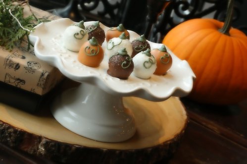A decorative cake stand with chocolate-covered treats shaped like pumpkins and acorns, alongside a small pumpkin.