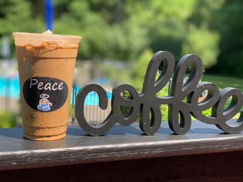 Iced coffee in a clear cup next to a wooden sign that says "Peace" and "coffee," with greenery in the background.