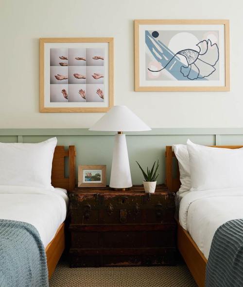 A cozy bedroom with two beds, a lamp, artwork on the walls, and a vintage trunk as a nightstand.