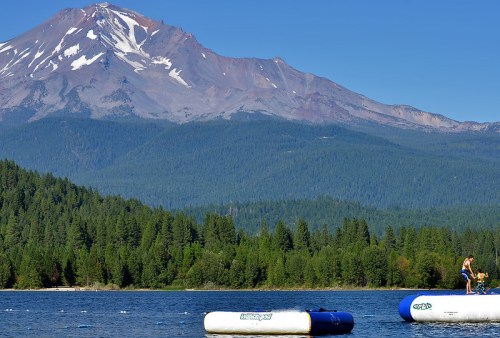 A serene lake scene with inflatable platforms, surrounded by lush forests and a majestic mountain in the background.