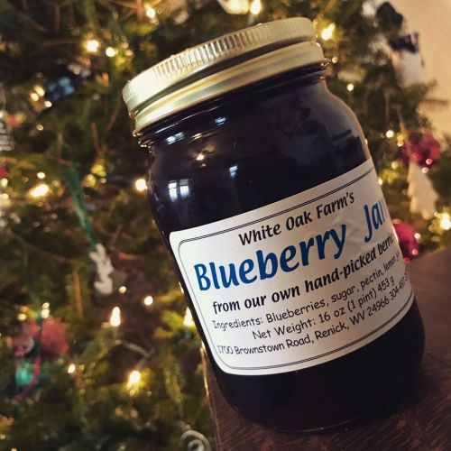 A jar of blueberry jam with a label detailing ingredients and the farm's name, set against a cozy background.