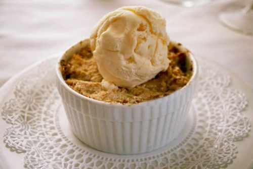 A ramekin filled with baked dessert topped with a scoop of vanilla ice cream on a decorative plate.
