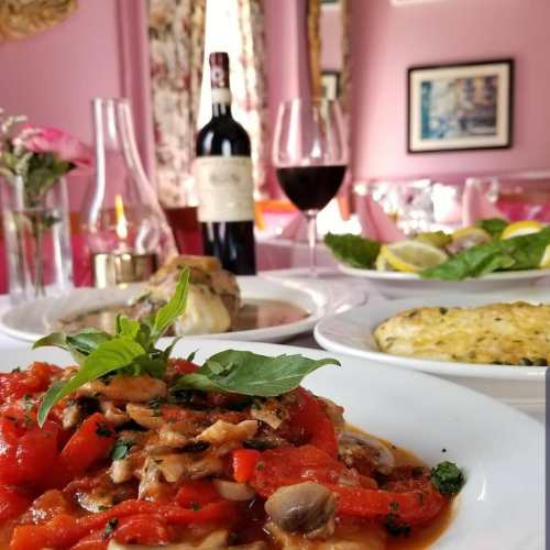 A vibrant plate of pasta with tomatoes and basil, accompanied by wine and elegant dining decor in a pink setting.