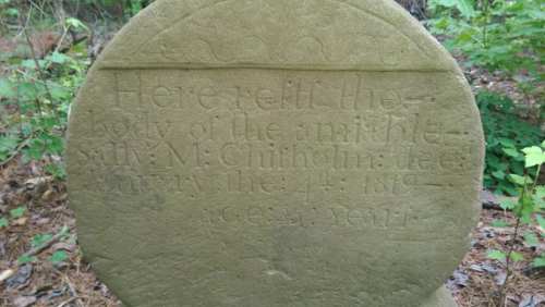 Weathered gravestone in a wooded area, inscribed with "Here rests the body of the amiable M. Chithem, died 1812."