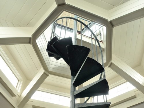 Spiral staircase viewed from below, leading up to a bright, octagonal ceiling with windows.
