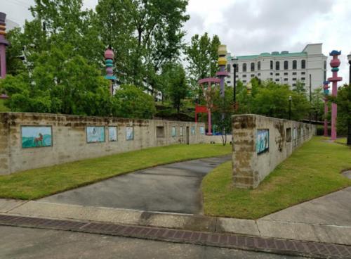 A park with colorful sculptures, grassy areas, and murals on concrete walls under a cloudy sky.