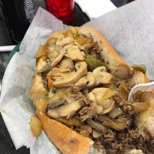 A close-up of a loaded sandwich with beef, sautéed onions, peppers, and mushrooms on a hoagie roll.