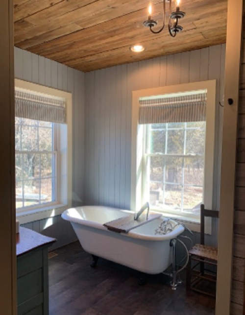 Bright bathroom featuring a vintage bathtub, wooden ceiling, and large windows with natural light.