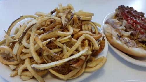 A plate of golden, crispy curly fries next to a sandwich topped with ground beef, onions, and ketchup.