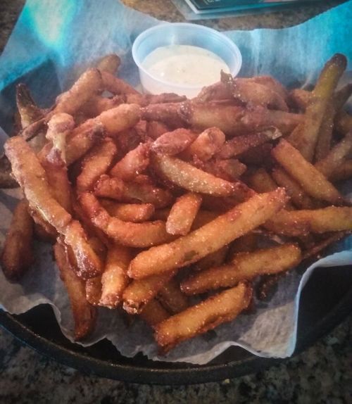A basket of golden-brown fries served with a small cup of dipping sauce.
