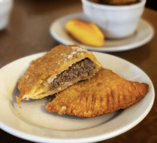 A golden-brown empanada cut in half, revealing a savory beef filling, served on a white plate.