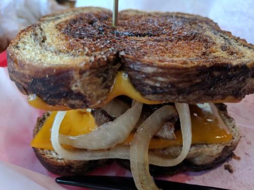A close-up of a grilled sandwich with melted cheese, onions, and crispy bread, held together with a toothpick.