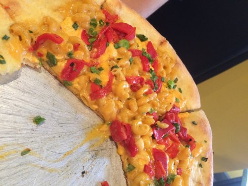A close-up of a pizza topped with macaroni, red peppers, and green onions on a golden crust.