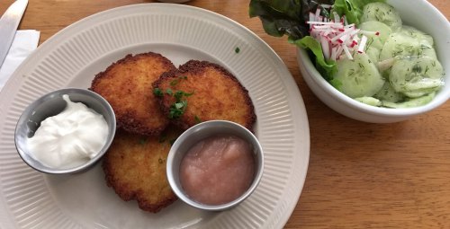Three golden-brown potato pancakes on a plate, served with sour cream and applesauce, alongside a fresh salad.