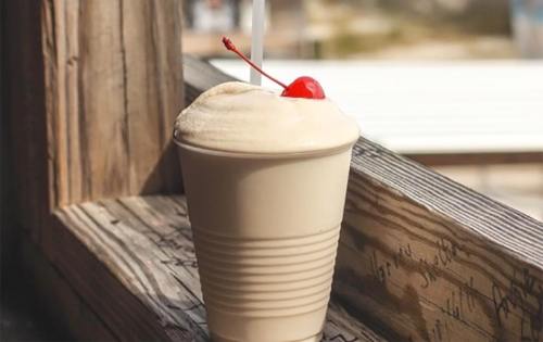 A frothy drink topped with a cherry, sitting in a cup on a wooden windowsill.