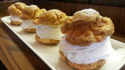 Four large cream puffs filled with whipped cream, dusted with powdered sugar, arranged on a tray.