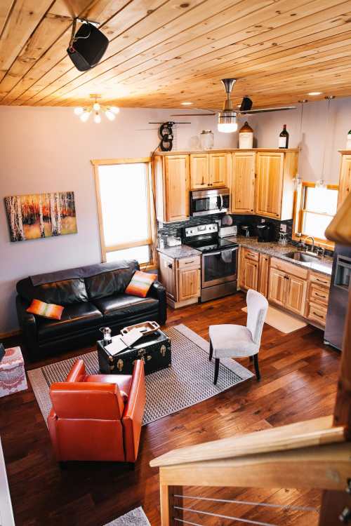 Cozy kitchen and living area with wooden cabinets, leather sofa, and stylish chairs in a warm, inviting space.