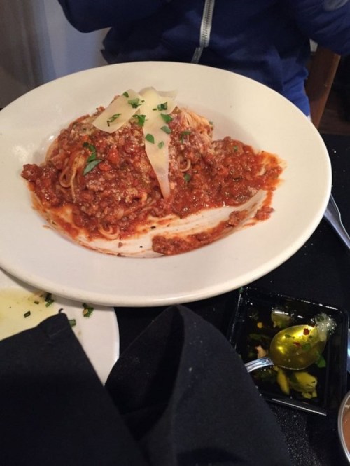 A plate of spaghetti topped with meat sauce and cheese, accompanied by a small dish of olive oil and herbs.