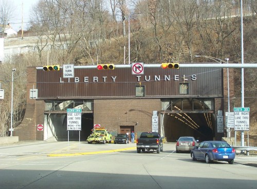 Entrance to the Liberty Tunnels, featuring traffic signals and signage, surrounded by a hilly landscape.