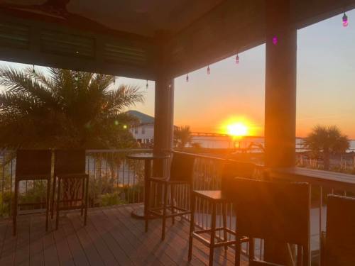 Sunset view from a deck with bar stools, palm trees, and colorful lights, overlooking a serene waterfront.