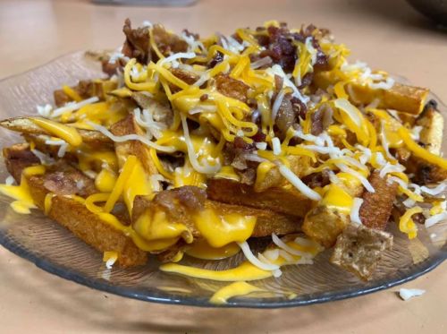A plate of loaded fries topped with melted cheese, bacon bits, and shredded cheese.