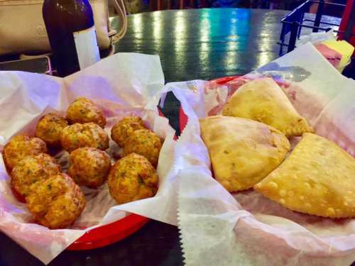 A red tray with two types of fried snacks: golden-brown fritters and crispy pastries, served with parchment paper.