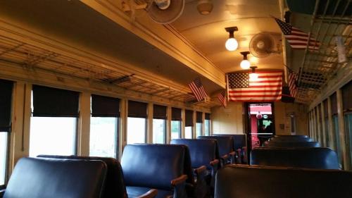 Interior of a vintage train car with blue seats and small American flags hanging from the ceiling.