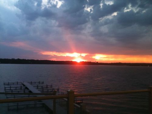 A vibrant sunset over a lake, with clouds and a silhouette of a dock in the foreground.