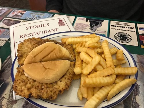A plate with two breaded chicken patties on buns and a side of crinkle-cut fries, with a restaurant menu in the background.