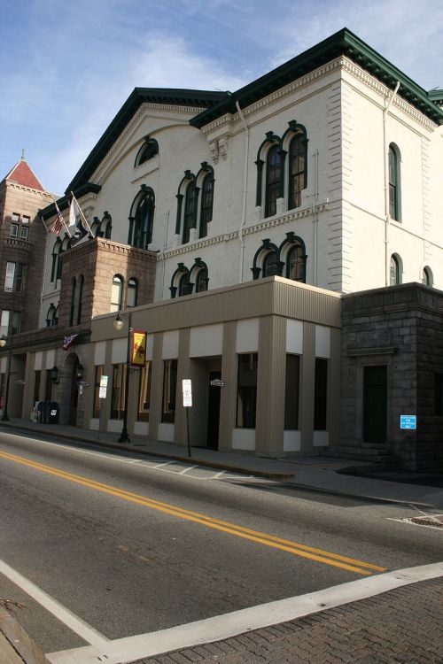 Historic building with arched windows and a decorative facade, located on a city street with parked cars.