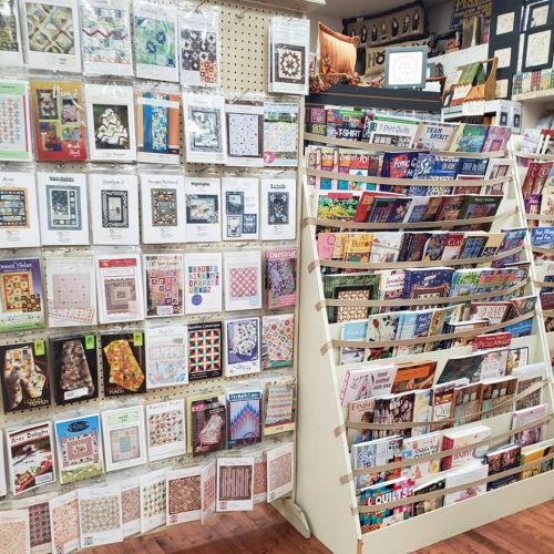 A craft store display featuring various quilting patterns and magazines on shelves and walls.