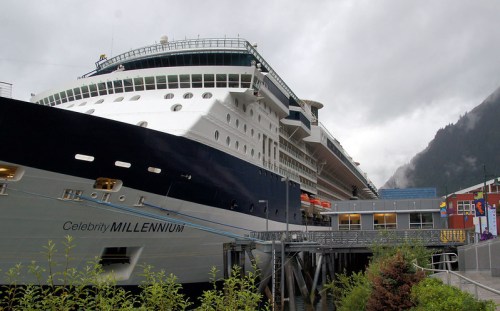A large cruise ship, Celebrity Millennium, docked at a port with cloudy skies and mountains in the background.