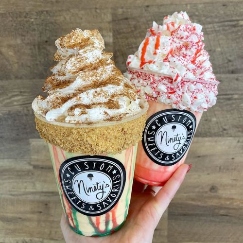 Two colorful dessert cups topped with whipped cream and garnishes, held in a hand against a wooden background.