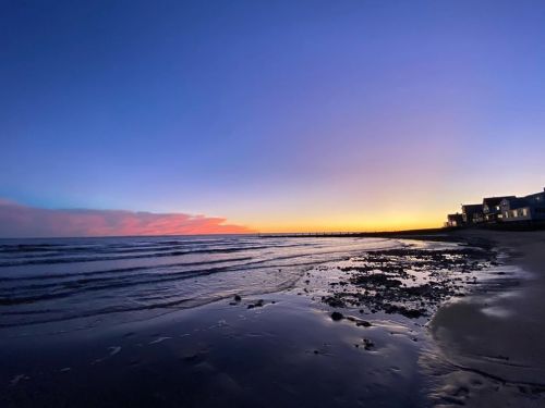 A serene beach at sunset, with calm waves and a colorful sky reflecting shades of blue and orange.