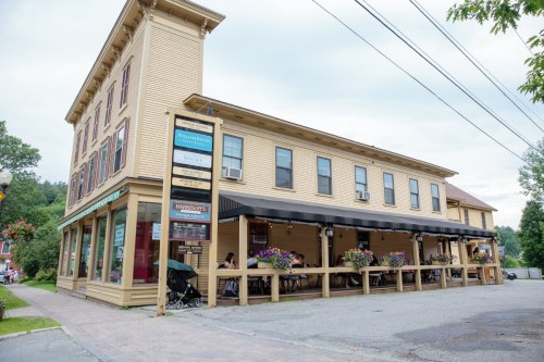 A charming yellow building with a covered porch, flower boxes, and signage for nearby businesses.