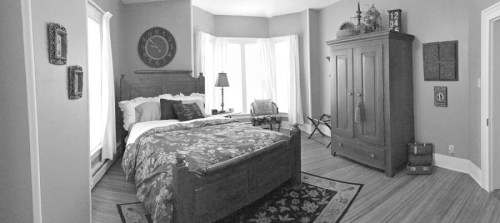 Cozy bedroom featuring a wooden bed, floral bedding, a large window, and vintage decor in a warm color palette.