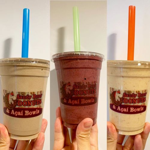 Three smoothie cups with colorful straws, featuring the logo of Sandy Pony Donuts & Açaí Bowls.