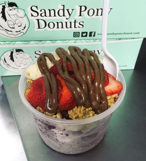 A cup of acai topped with granola, strawberries, banana slices, and drizzled with chocolate sauce.