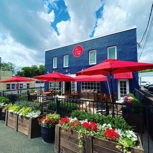 A blue café building with red umbrellas and flower planters outside, under a partly cloudy sky.