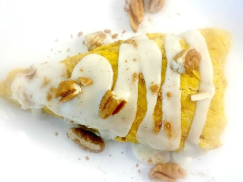 A golden omelette drizzled with white sauce and topped with pecans and a sprinkle of cinnamon.