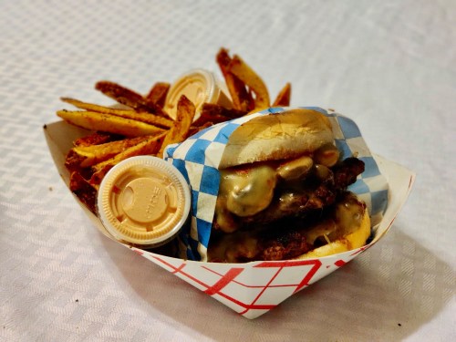 A delicious cheeseburger with toppings, served with a side of crispy fries in a red and white checkered tray.