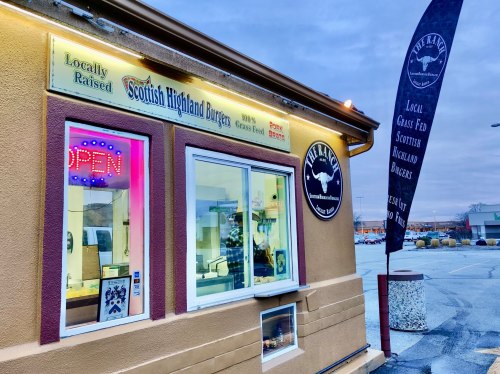 Exterior of a burger restaurant featuring a sign for Scottish Highland burgers and an "Open" neon light.