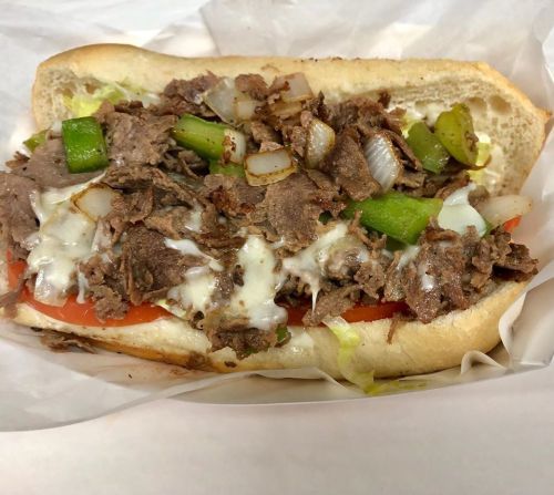 A loaded sandwich with sliced beef, onions, green peppers, tomatoes, and melted cheese on a hoagie roll.